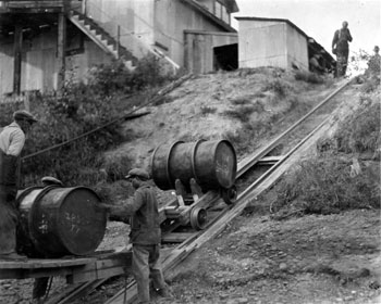 “Arriving at Mayo and unloading a barge of oil.” Two men operate a rail and trolley system used for unloading a barge of oil at the W.P.&Y.R. Freight Shed at Mayo. ca. 1933