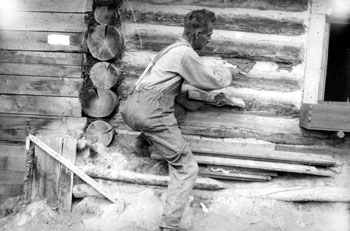 “The same job every fall.” 1929. While Mary made the home beautiful, Claude was responsible for keeping up the maintenance. Here he re-chinks the logs with a mud mixture to keep out winter drafts.